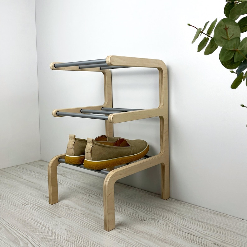 Pu&ograve; includere: Uno scarpiera in legno chiaro con tre ripiani e binari in metallo argentato. Due paia di scarpe marroni sono sullo scaffale inferiore.