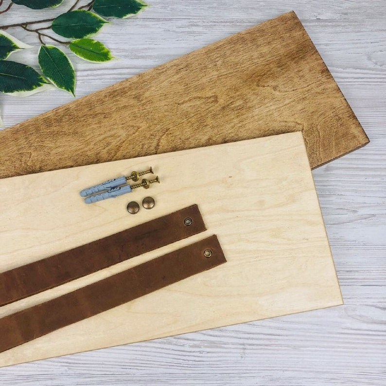 May include: Two brown leather straps with brass hardware, two gray plastic anchors, and two brass screws on a light wood surface.