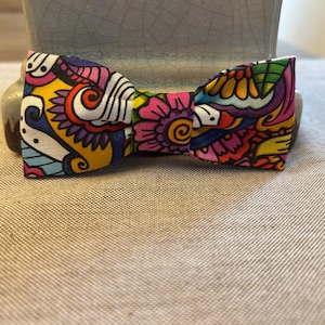 Può includere: Un papillon colorato con un motivo paisley in tonalità di rosa, giallo, blu, verde e viola.