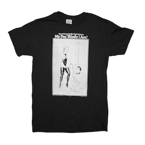May include: Black t-shirt with a white graphic print of a woman in a leather outfit holding a leash and a man kneeling on the floor. The text on the shirt reads "May I Always Be The Kind Of Person My Dog Thinks I Am!"