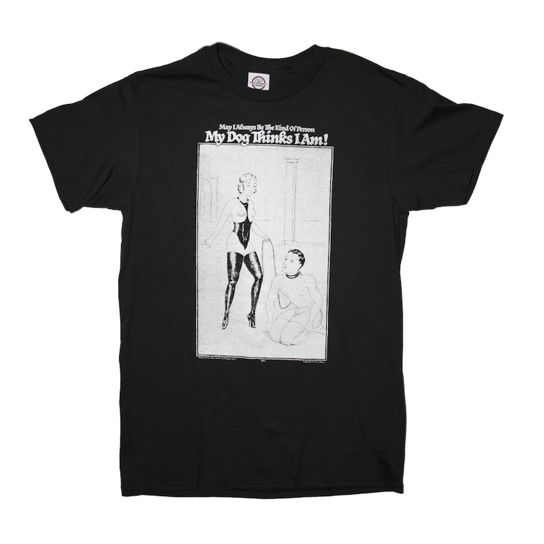 May include: Black t-shirt with a white graphic print of a woman in a leather outfit holding a leash and a man kneeling on the floor. The text on the shirt reads "May I Always Be The Kind Of Person My Dog Thinks I Am!"