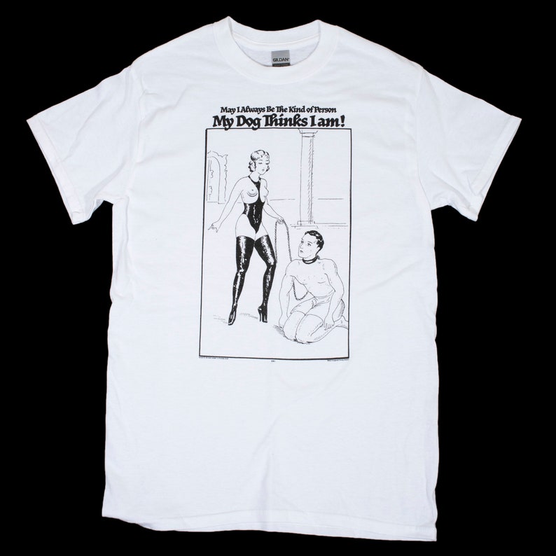 May include: White t-shirt with a black and white illustration of a woman holding a whip and a man kneeling. The text on the shirt reads "May I Always Be The Kind of Person My Dog Thinks I Am!"