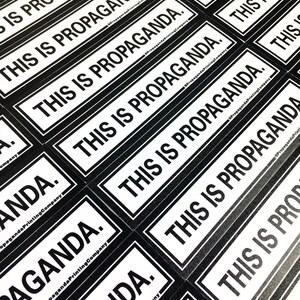 May include: Close-up of multiple black and white stickers with the text "This is Propaganda." printed on them. The stickers are arranged in a staggered pattern, with the text facing the viewer. The stickers are printed by Propaganda Printing Company.