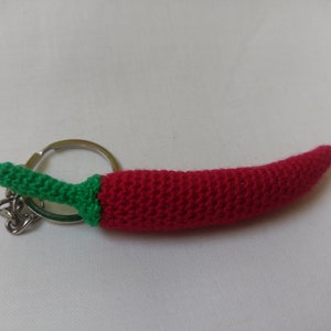 May include: A red and green crocheted chilli pepper keyring with a silver metal ring.
