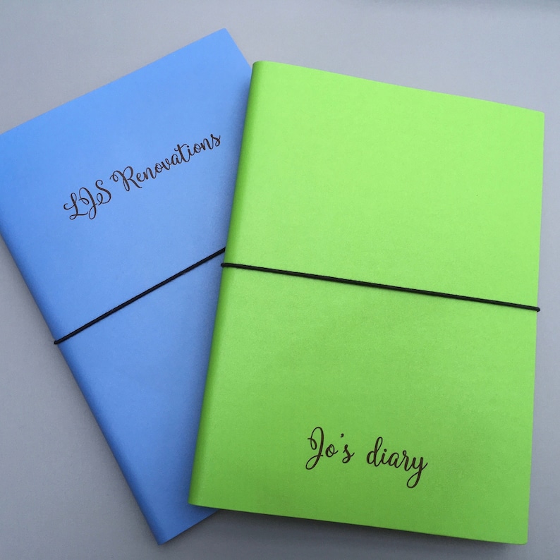 Pode incluir: Duas pastas, uma azul e outra verde, com el&aacute;sticos. A pasta azul tem o texto "LJS Renovations" impresso na frente. A pasta verde tem o texto "Jo's diary" impresso na frente.
