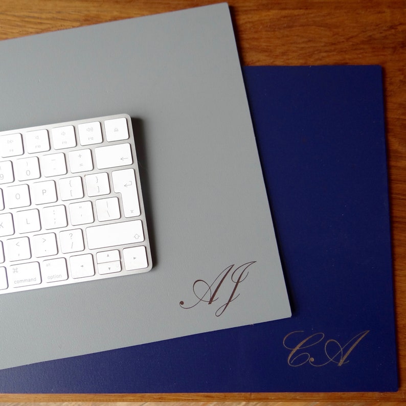 Może przedstawiać: Dwie szare i niebieskie podkładki pod mysz z personalizowanymi inicjałami. G&oacute;rna podkładka ma inicjały "AJ", a dolna podkładka ma inicjały "CA".