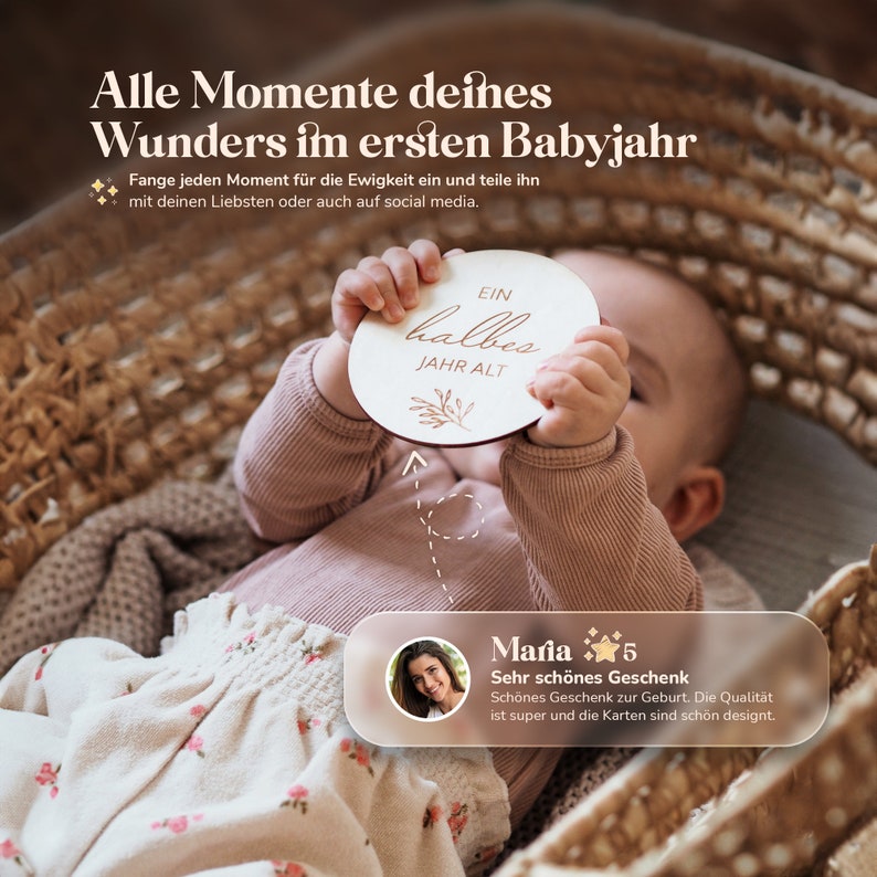 May include: A baby holding a wooden sign that says "Ein halbes Jahr alt" (One half year old). The sign is round and has a light brown background with gold lettering. The baby is wearing a pink shirt and a floral skirt.