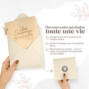 Op de afbeelding: Een houten kaart met de tekst "Une Surprise POUR VOUS" in een cr&egrave;me-kleurige envelop. De kaart wordt in de hand van een persoon gehouden. De afbeelding toont ook een tweede envelop met een hartsymbool.