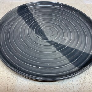 Può includere: Un piatto in ceramica grigia con un design a spirale e una striscia nera al centro.