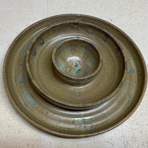 Könnte beinhalten: Ein Set aus drei handgefertigten Keramik-Servierschalen. Das Set beinhaltet einen großen Teller, einen mittelgroßen Teller und eine kleine Schüssel, alle in einem gedämpften Olivgrün mit blauen Akzenten. Die Teller und die Schüssel sind ineinander verschachtelt.