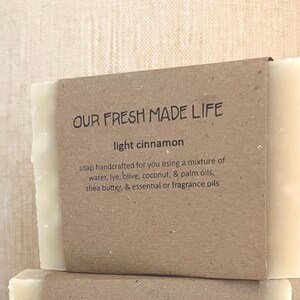 May include: A bar of light cinnamon soap with a brown paper label. The label reads "OUR FRESH MADE LIFE" and "light cinnamon." The text below describes the soap's ingredients, including water, lye, coconut, and shea butter.