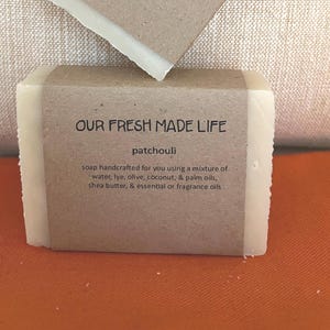 May include: A bar of patchouli soap with a brown paper label that reads "OUR FRESH MADE LIFE." The label also lists ingredients like water, lye, olive oil, coconut oil, palm oils, shea butter, and essential oils.