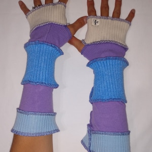 May include: A pair of fingerless gloves with a layered design. The gloves are made of a soft, stretchy fabric and feature a white, purple, and blue color scheme. The gloves have a small tag on the back of the hand that says "T&R".