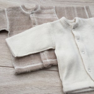 May include: Two baby onesies, one in a light brown colour and one in white. Both onesies have a button closure down the front.