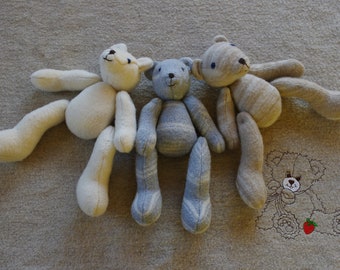 May include: Three handmade teddy bears made from fabric scraps. The bears are sitting on a beige blanket. One bear is white, one is light blue and white striped, and one is beige and white striped.