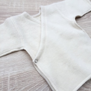 Peut inclure: Une grenouillère blanche à manches courtes pour bébé, de style enveloppant, avec une fermeture à pression.