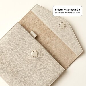 May include: A light gray leather case with a hidden magnetic flap and a minimalist design. The case is open, revealing a beige interior and a button closure. The text "Hidden Magnetic Flap, Seamless, minimalist look" is visible.