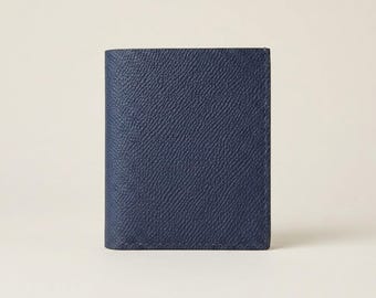 May include: A navy blue bifold wallet featuring a distinct cross-hatch textured surface. The wallet is rectangular in shape with clean, straight edges and visible stitching along the perimeter, showcasing a uniform and solid dark blue color throughout.