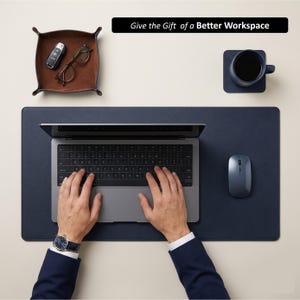 Pode incluir: Uma vista de cima de um espaço de trabalho com um tapete de secretária azul marinho, um laptop, um rato e uma bandeja de couro castanho com chaves e óculos. Uma caneca azul marinho com café num descanso de copo a condizer. Texto: Dê o presente de um melhor espaço de trabalho.