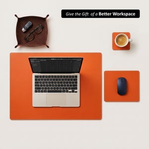 May include: An orange leather desk mat with a laptop, mouse, and coaster. A brown leather tray holds glasses and a car key. The image includes the text: "Give the Gift of a Better Workspace."
