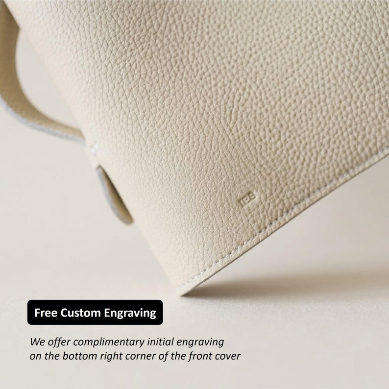 May include: Close-up of a cream-colored leather bag with a textured surface. The bag has a handle and a small, embossed "JEB" logo. The image includes the text "Free Custom Engraving".