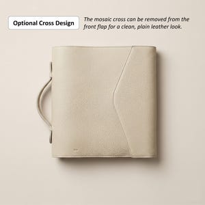 May include: A cream-colored leather portfolio with a handle and a flap. The text "Optional Cross Design" and "The mosaic cross can be removed from the front flap for a clean, plain leather look" are visible. The portfolio has a textured surface.