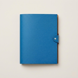 Può includere: Un diario in pelle blu con una superficie strutturata. Il diario ha un dorso marrone e una chiusura a scatto. Il diario è chiuso e sembra nuovo.
