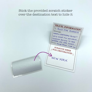 May include: A white card with the text "TRAVEL INFORMATION" and a message that says "HAPPY BIRTHDAY ALICE!! LETS SHOP TILL WE DROP... SCRATCH BELOW TO SEE WHERE WE ARE GOING... From: YOUR MAN, TOM xx". The card also has a scratch-off area that says "SCRATCH HERE FOR DESTINATION" and the text "NEW YORK" underneath.