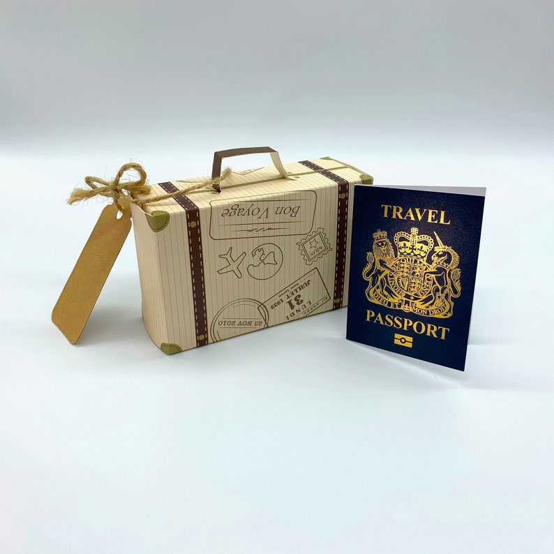 May include: A small, brown cardboard suitcase with a gold handle and a tag that says "Bon Voyage". The suitcase is next to a blue passport with gold lettering that says "Travel Passport".
