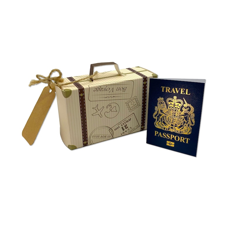 May include: A small, brown cardboard suitcase with a luggage tag and a blue passport with gold lettering that says "TRAVEL PASSPORT". The suitcase has the words "Bon Voyage" printed on it.