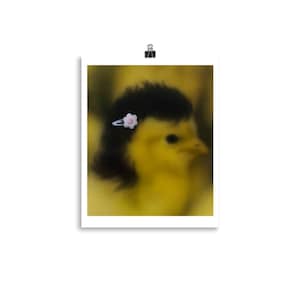 Può includere: Un pulcino giallo con un design nero simile ai capelli e una piccola forcina a forma di fiore bianco. Il pulcino è ambientato su uno sfondo giallo sfocato. L'immagine è una stampa.