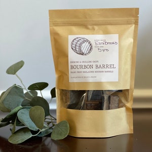 Puede incluir: Una bolsa de papel marrón con una ventana transparente que muestra virutas de madera para ahumar. La bolsa tiene una etiqueta con el texto "Ezra Brooks 5yrs" y "Bourbon Barrel" impreso en ella.