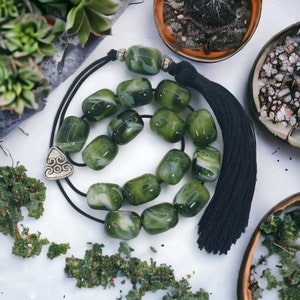 Può includere: Un collana di preghiera verde e bianca con un fiocco nero. Le perle sono di vetro e hanno un motivo a spirale. La collana è infilata su un cordoncino nero.