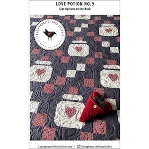 May include: A quilted blanket with a repeating pattern of jars with hearts on a dark blue background. The text "Love Potion No. 9" is at the top. A red heart-shaped pillow is in the bottom right corner. The blanket has a decorative stitch pattern.