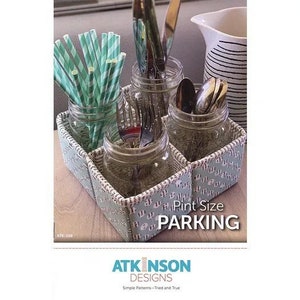 May include: A sewing pattern for a pint-sized parking organizer. The pattern is for a small, square organizer made of fabric and has a green and white design. The organizer is designed to hold jars or other containers, and the pattern includes instructions for making the organizer.