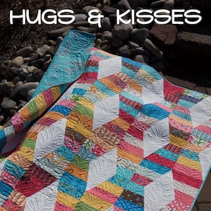 May include: A colorful quilt with a geometric pattern of white diamonds and colorful squares. The quilt is made with a variety of fabrics, including floral prints, stripes, and solids. The quilt is laid out on a patio with a stone surface. The quilt is titled "Hugs & Kisses" and the maker's name is "Jaybird Quilts".
