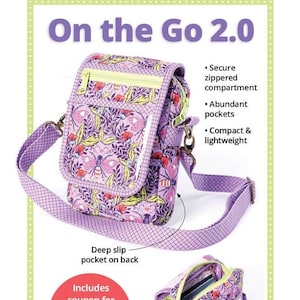 May include: Purple and green fabric crossbody bag with a zippered compartment, a deep slip pocket on the back, and a clear plastic window. The bag is designed for travel and has the text "On the Go 2.0" and "byannie.com" printed on it.
