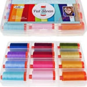 Pode incluir: Um conjunto de caixas de plástico transparente contendo bobinas de linha coloridas. A tampa da caixa apresenta o texto "The Perfect Box of Colors" e o nome "Pat Sloan". As bobinas de linha são dispostas em fileiras, exibindo uma variedade de cores vibrantes.