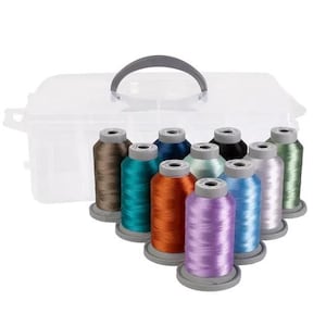 Puede incluir: Una caja de almacenamiento de plástico transparente con un asa gris contiene carretes de hilo de bordar de colores. Los colores del hilo incluyen marrón, turquesa, naranja, morado, azul y verde. Los carretes están colocados delante de la caja.