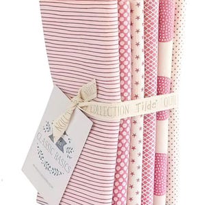 Peut inclure: Un ensemble de tissus roses avec divers motifs, dont des rayures, des pois et des étoiles. Les tissus sont liés par un ruban avec l'inscription "Tilda's Quilts Collection". Une étiquette "Classic Basics" est attachée.