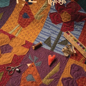 May include: A quilt with a patchwork design featuring a red flower, a bird, and a heart. The quilt is made of various fabrics in shades of red, orange, yellow, green, blue, and purple. The quilt is titled "Crazy Favorite Things" and is made by "One Sister".