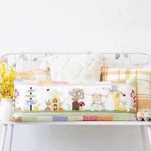 May include: A colorful embroidered pillow with a bunny theme. The pillow features a house, a carrot, a mushroom, and a sign that says "Hoppin' Down the Bunny Trail".