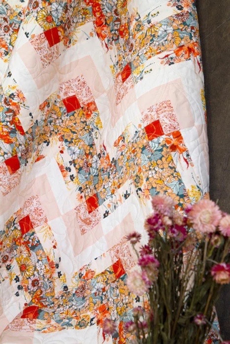 May include: A floral quilt with a white background and a geometric pattern. The quilt features a variety of colorful flowers in shades of orange, yellow, and blue. The quilt's design includes red squares and pink stripes.