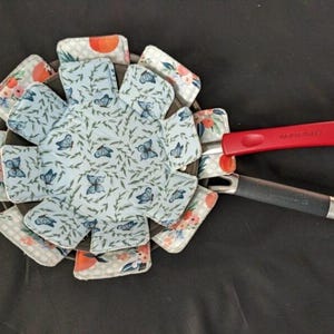 May include: A blue and white fabric pot holder with a butterfly pattern. The pot holder is folded into a circle shape and has a red handle.