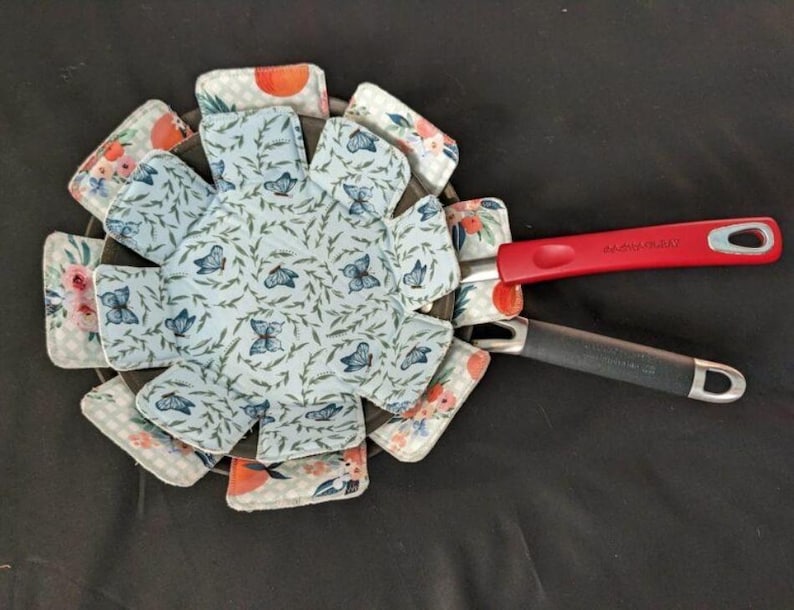 May include: A blue and white fabric pot holder with a butterfly pattern. The pot holder is folded into a circle shape and has a red handle.