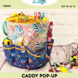 May include: A fabric caddy with a blue handle and multiple pockets. The caddy has a colorful swirl pattern on the inside and a blue patterned exterior with yellow trim. The text "CADDY POP-UP" is visible, along with the dimensions 5.5" D x 6" H.