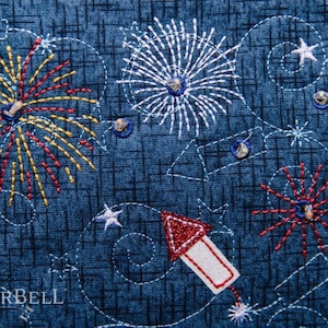 May include: Embroidered fabric with a blue background and white, red, and yellow fireworks designs. The fabric also features a red and white rocket design and the text "KIMBERBELL".