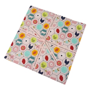 May include: A stack of fabric squares with a repeating pattern of farm animals, strawberries, and flowers in a honeycomb design. The fabric is light pink with accents of yellow, green, and blue. A ribbon with the text "Poppie Cotton sunshine and joy in every detail" is wrapped around the squares.
