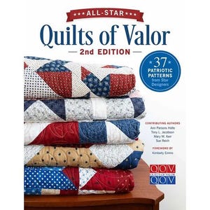 May include: A book titled All-Star Quilts of Valor 2nd Edition featuring a stack of five folded quilts with red, white, and blue star-themed fabric patterns. The cover includes text about 37 patriotic patterns and lists contributing authors.