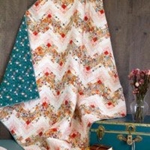 May include: A white ceramic mug with a black handle and the text "But First, Coffee" in a bold, black font. The mug is set against a blurred background, suggesting a cozy setting.